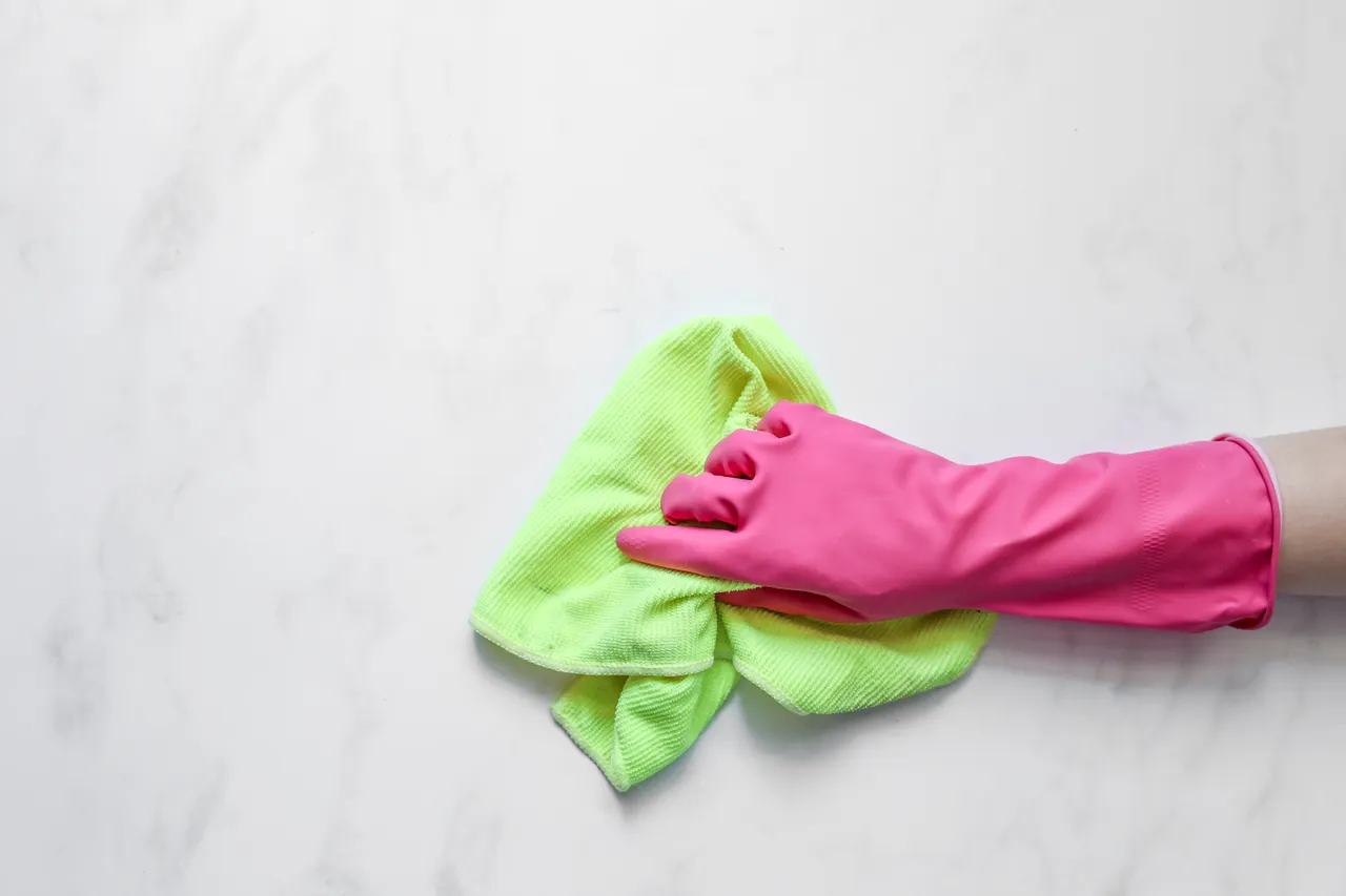 A hand in a pink rubber glove wiping a surface with a green cloth
