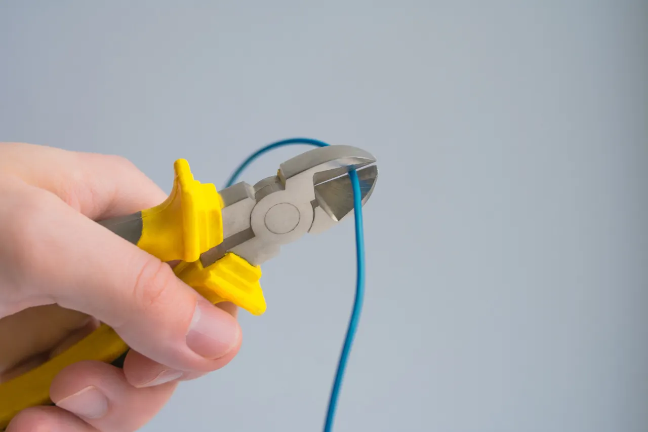 A hand holding yellow-handled cutting pliers around a blue wire