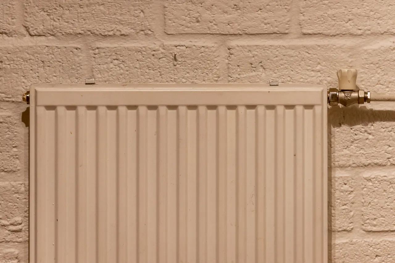A white heating radiator mounted against a textured brick wall