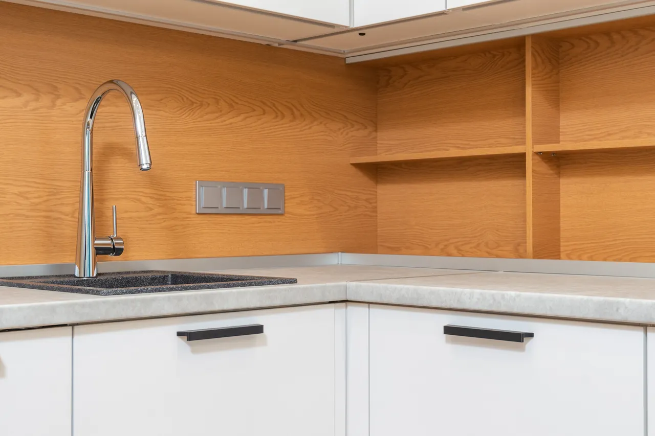 A chrome kitchen faucet above a dark sink beside wooden shelves