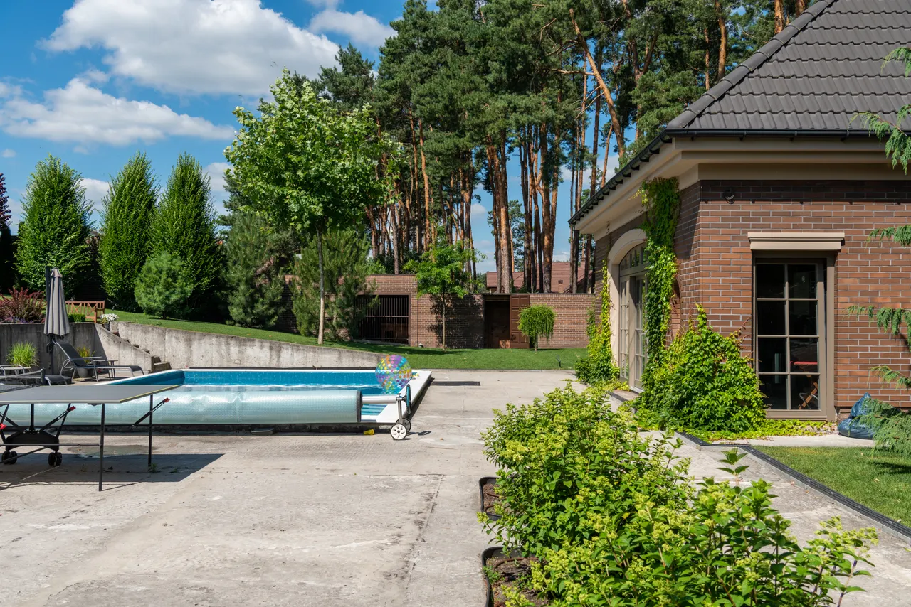 An outdoor swimming pool beside a brick house and landscaped yard