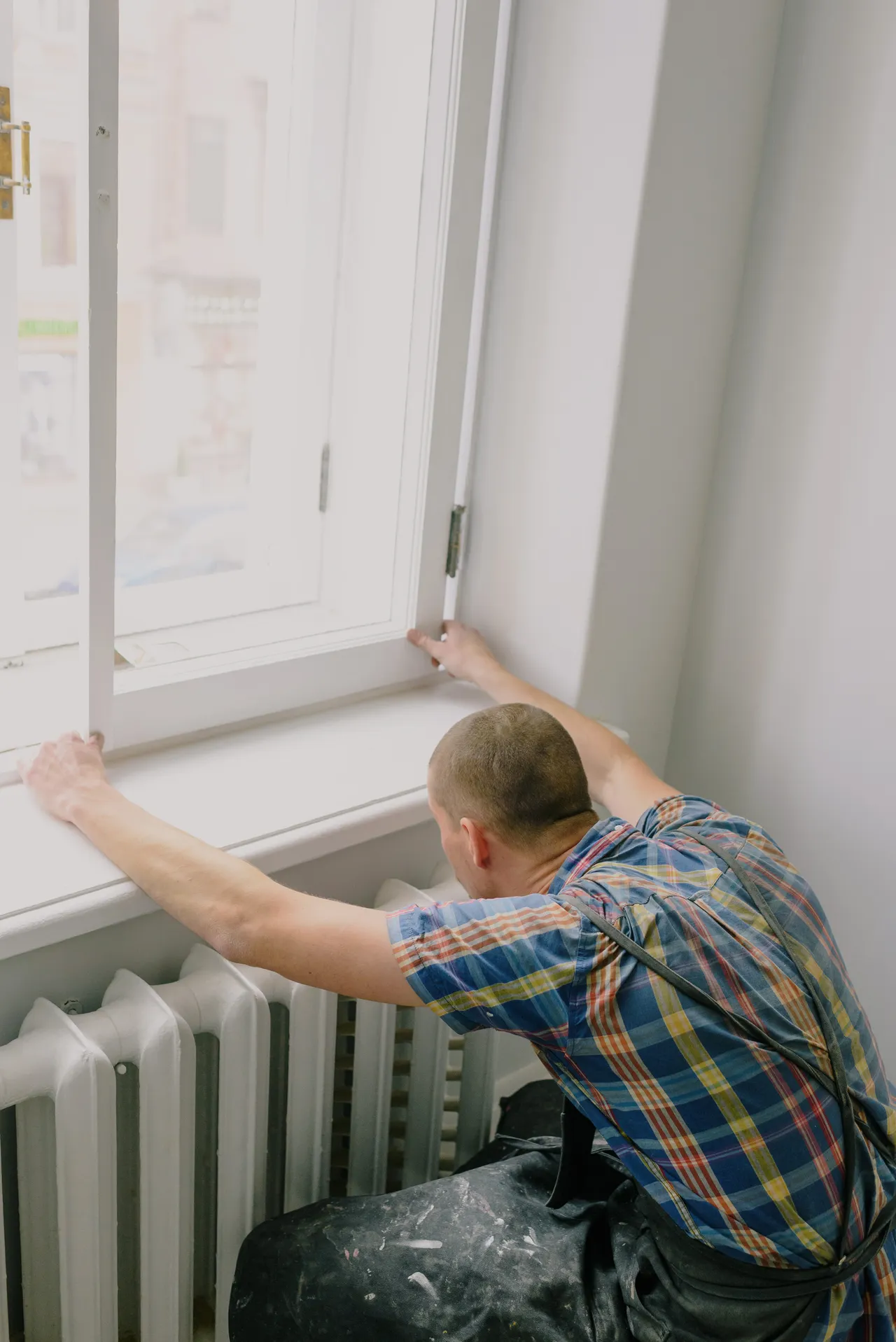 A worker fitting a white window frame above a radiator