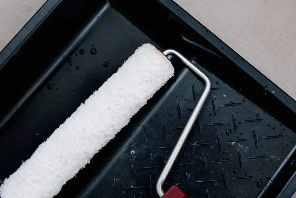 A white paint roller resting diagonally in a black paint tray