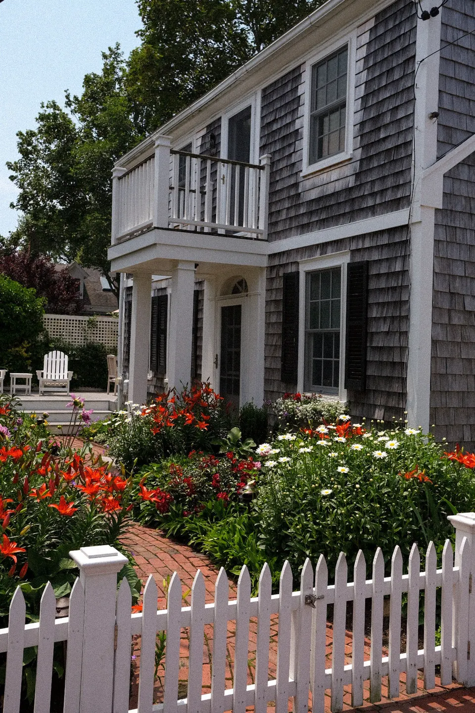 A shingled Nantucket house, porch, flower garden and white picket fence